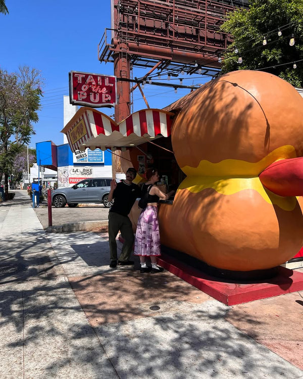 People standing at the Tail O’ The Pup hot dog stand in Los Angeles with the iconic hot dog-shaped building.