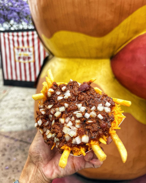 Basket of Tail O' The Pup chili cheese fries held in front of the iconic hot-dog-shaped stand in West Hollywood.