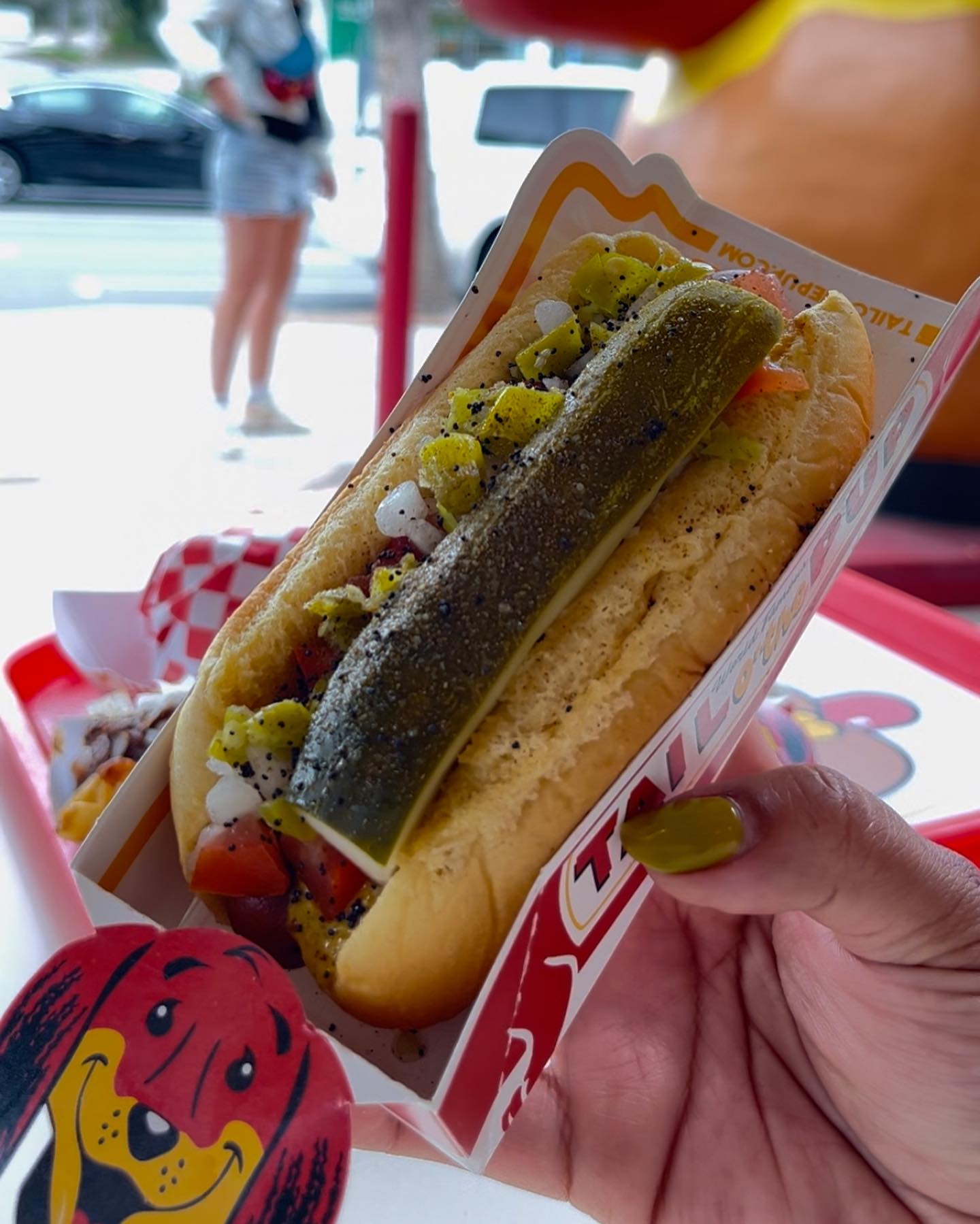 A woman holding a Chicago-style Hot Dog from Tail O’ The Pup.