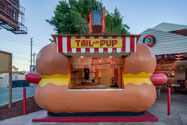 Tail O' The Pup's iconic hot-dog-shaped food stand in Los Angeles under a blue sky.